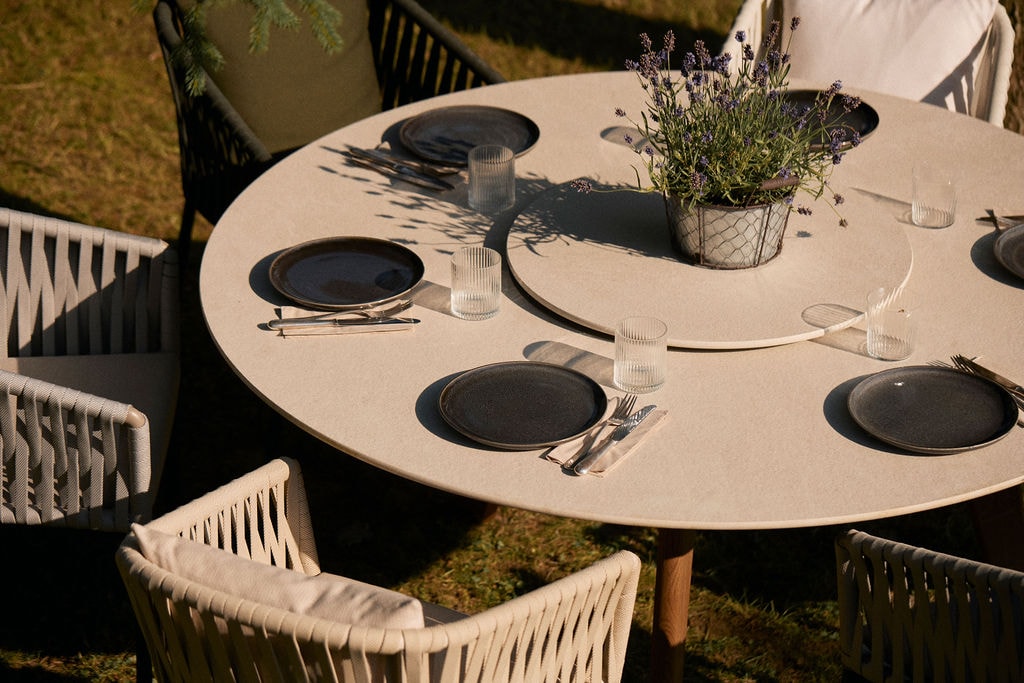 Menschen sitzen um einen runden Grilltisch, kochen gemeinsam und genießen die Atmosphäre im Freien.